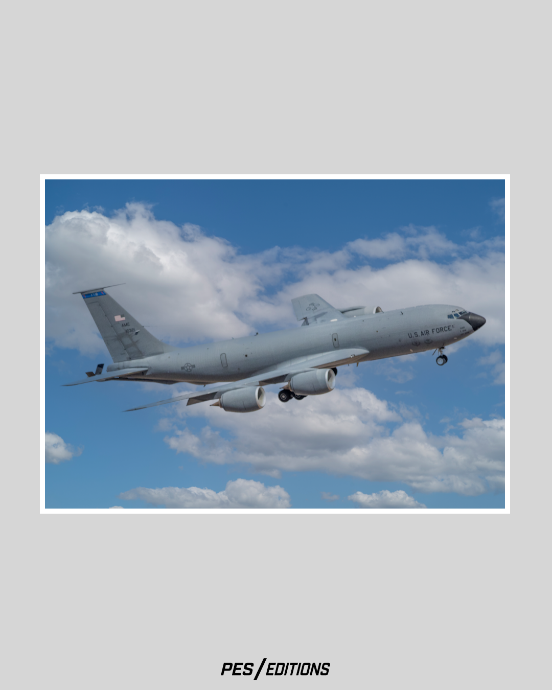 A detailed color photograph of a Boeing KC-135 Stratotanker in flight against a bright blue sky with scattered white clouds. The aircraft is captured from a side profile as it descends on approach with landing gear down.