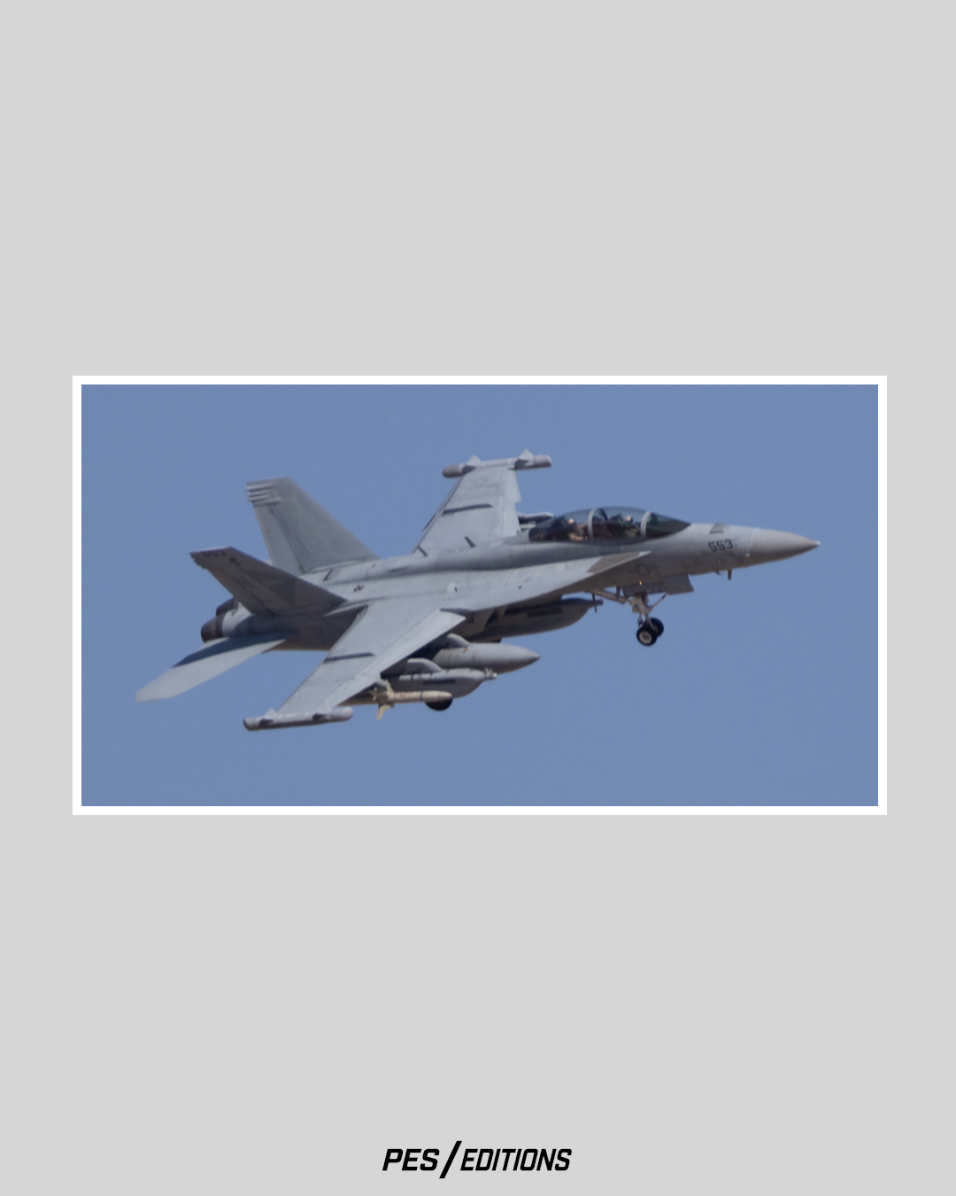 A detailed color photograph of a grey U.S. Navy F/A-18F Super Hornet (twin-seat tactical jet) in tactical flight against a dark blue sky.