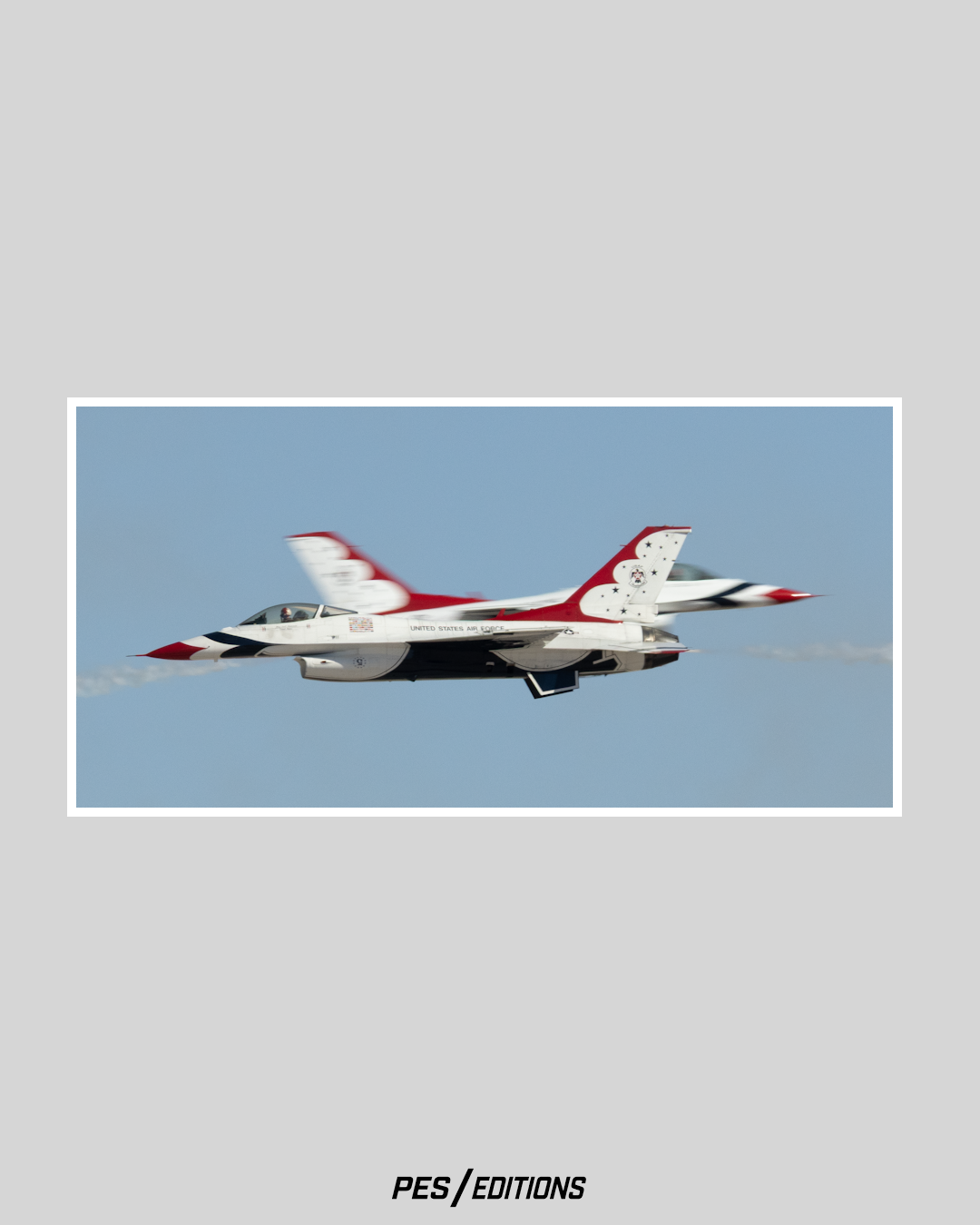 Two U.S. Air Force Thunderbirds F-16 jets crossing paths in a high-speed maneuver, with the foreground jet in sharp focus and the background jet blurred against a blue sky.