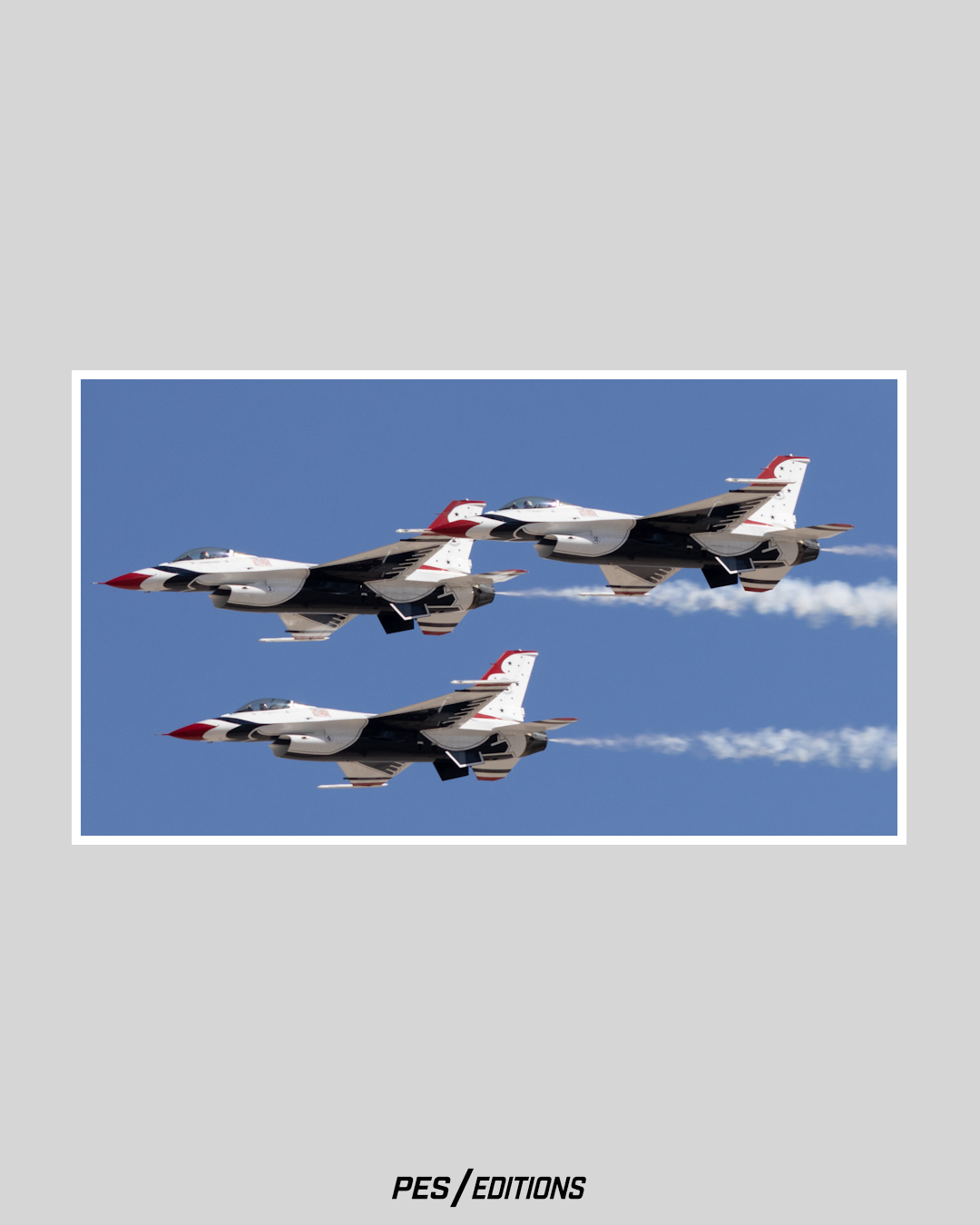 Three U.S. Air Force Thunderbirds F-16 fighter jets flying in a tight, stepped formation against a clear blue sky, leaving white smoke trails behind them.